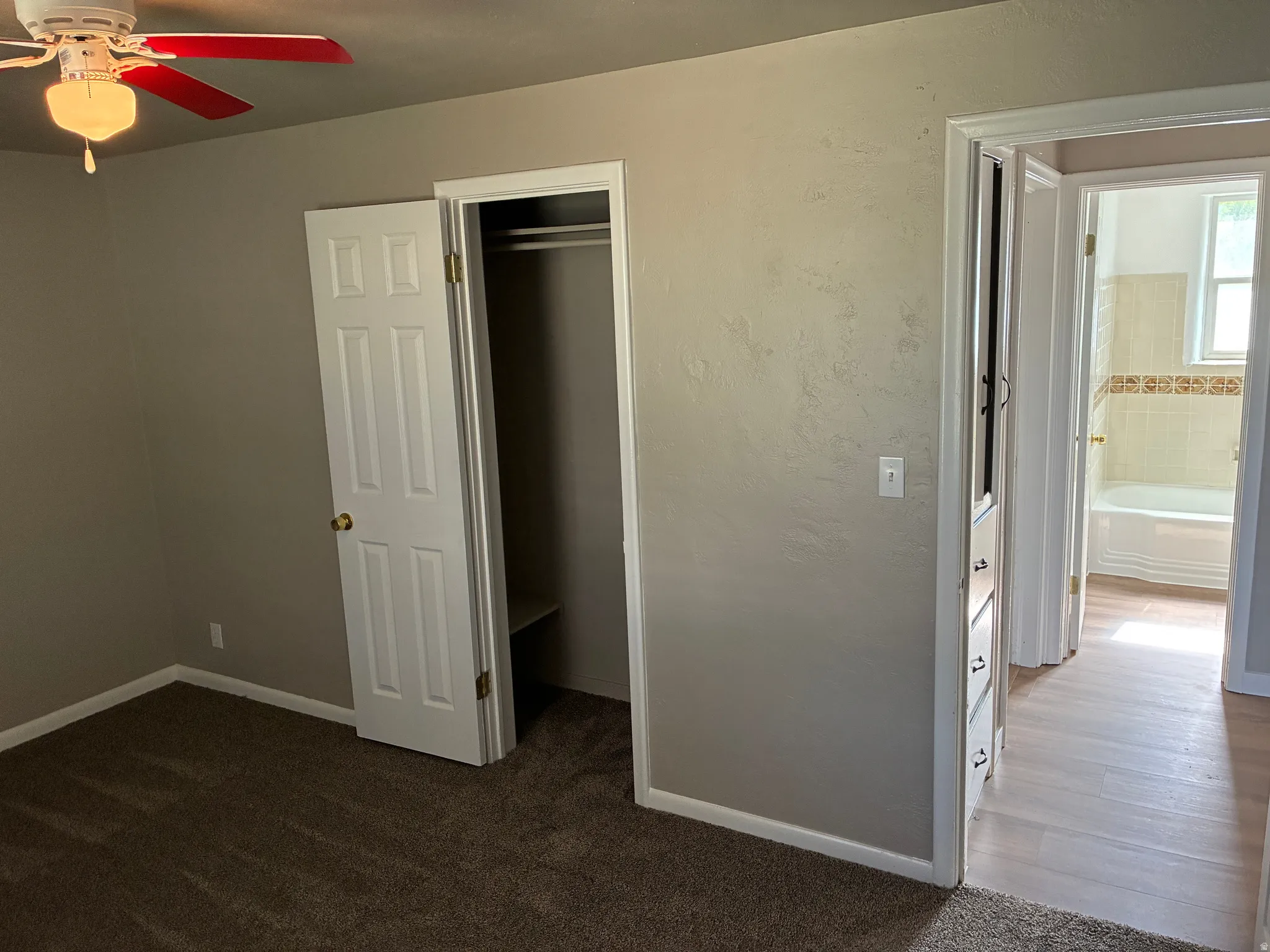 Room featuring textured walls, brown carpet flooring, and a ceiling fan with red blades