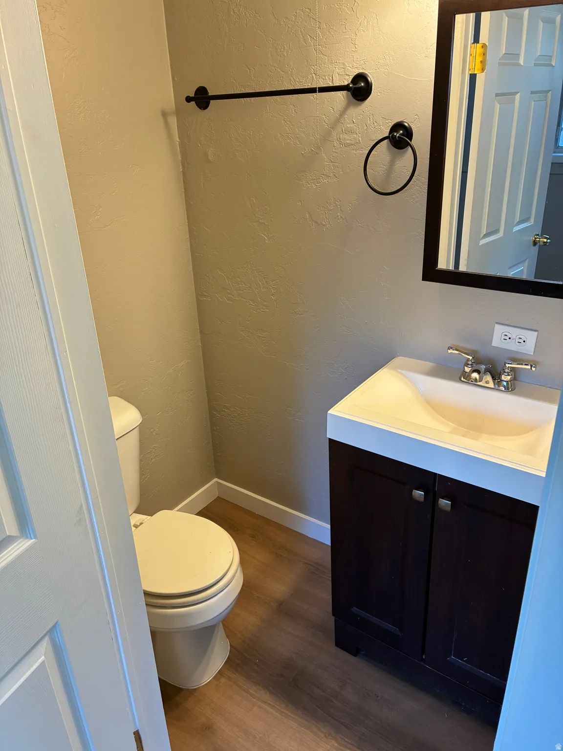 Compact bathroom featuring a dark wood-finish vanity with an integrated sink, chrome faucet, and wood-finish flooring