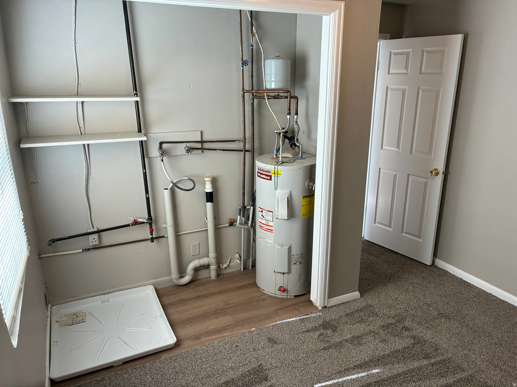 Utility closet featuring a water heater, built-in shelving, and wood-finish flooring