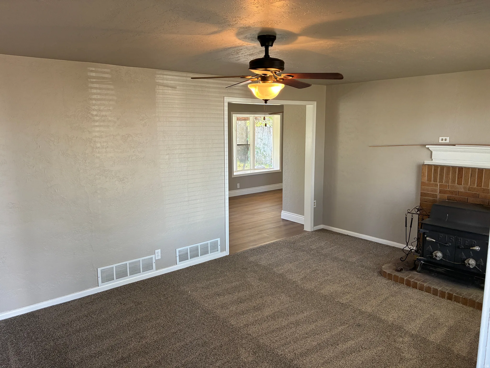 Living area featuring a brick fireplace with a wood-burning stove, brown carpeting, and a ceiling fan with integrated lighting