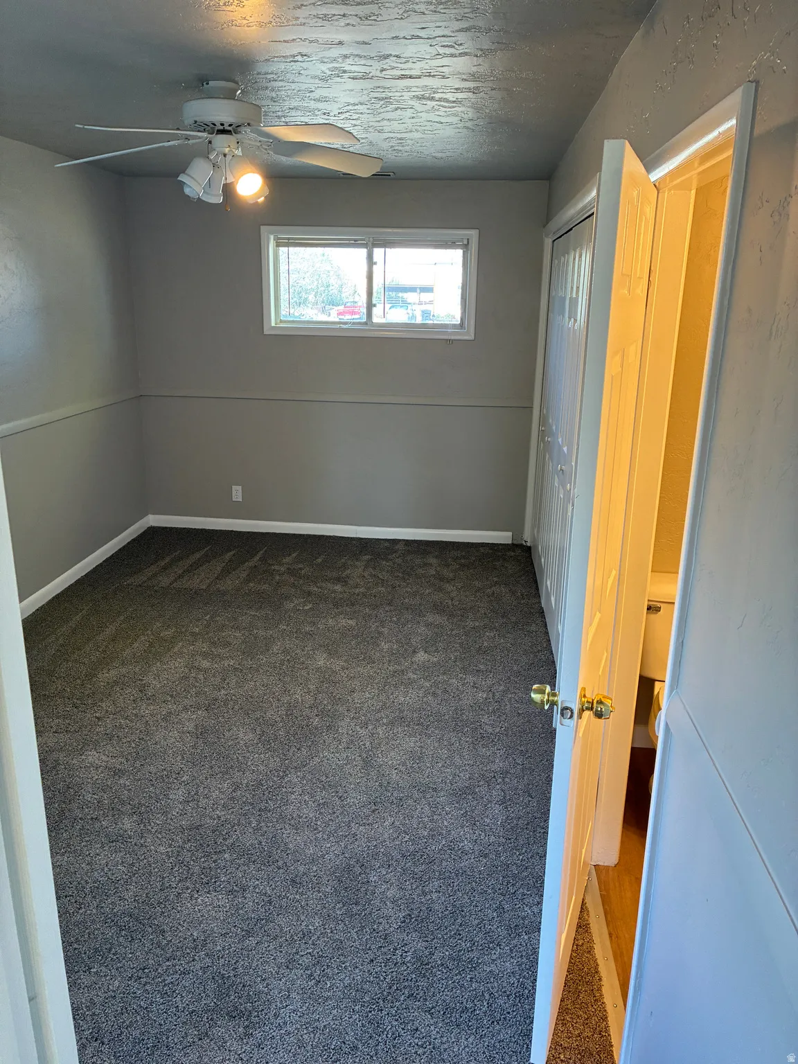 Room featuring gray wall paint, textured ceiling, a ceiling fan with integrated lighting, new carpeting, and a window with horizontal blinds