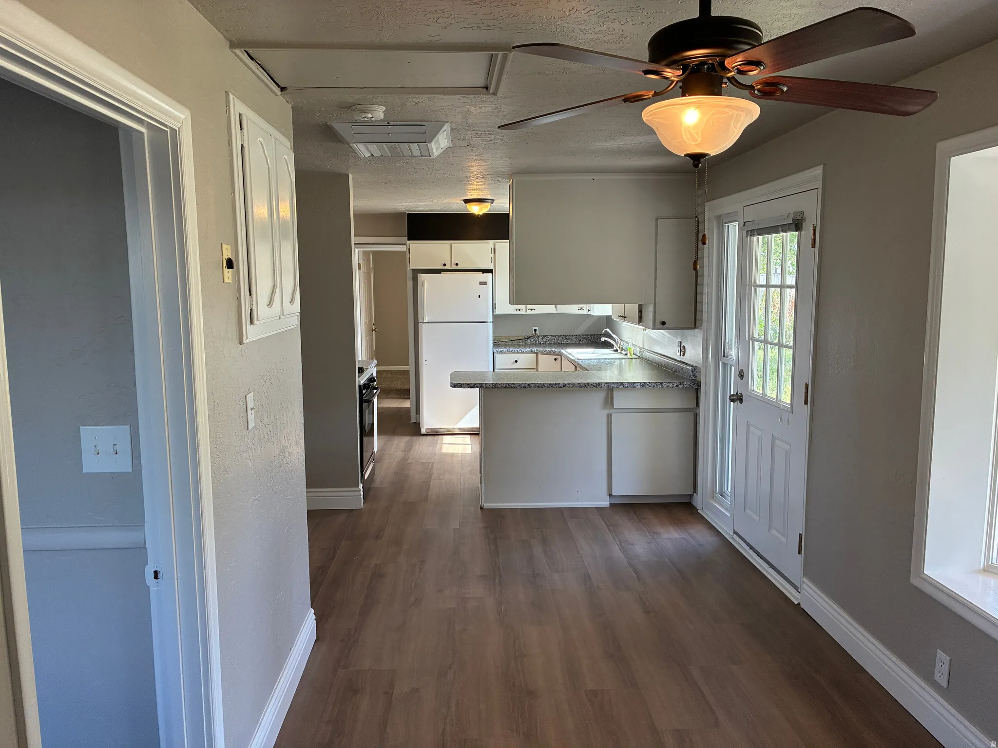 Kitchen and dining area featuring wood-finish flooring, a ceiling fan with integrated lighting, white cabinetry, a white refrigerator, and a door with glass panels