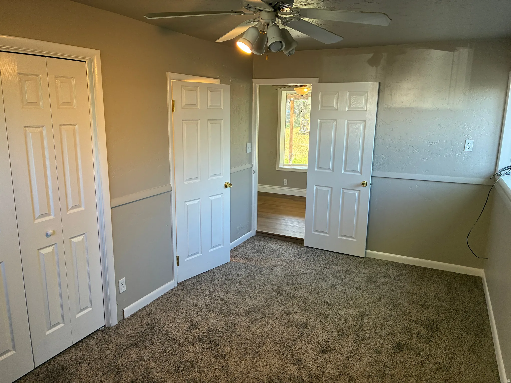 Carpeted room featuring a ceiling fan with integrated lighting, bi-fold closet doors, a six-panel door, and neutral wall tones