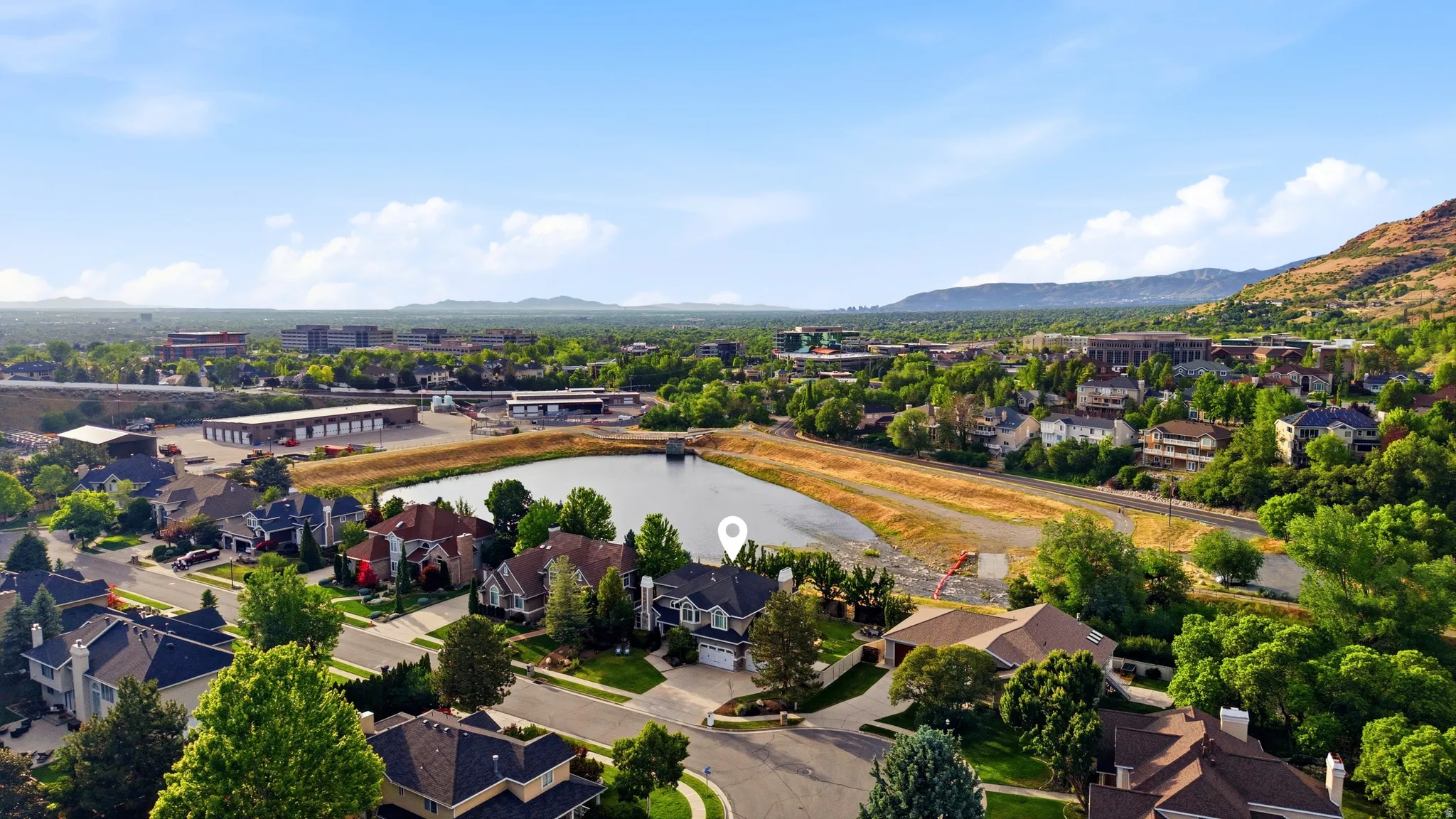 Aerial perspective showcasing a residential neighborhood with diverse architectural styles, mature trees, and a central pond feature