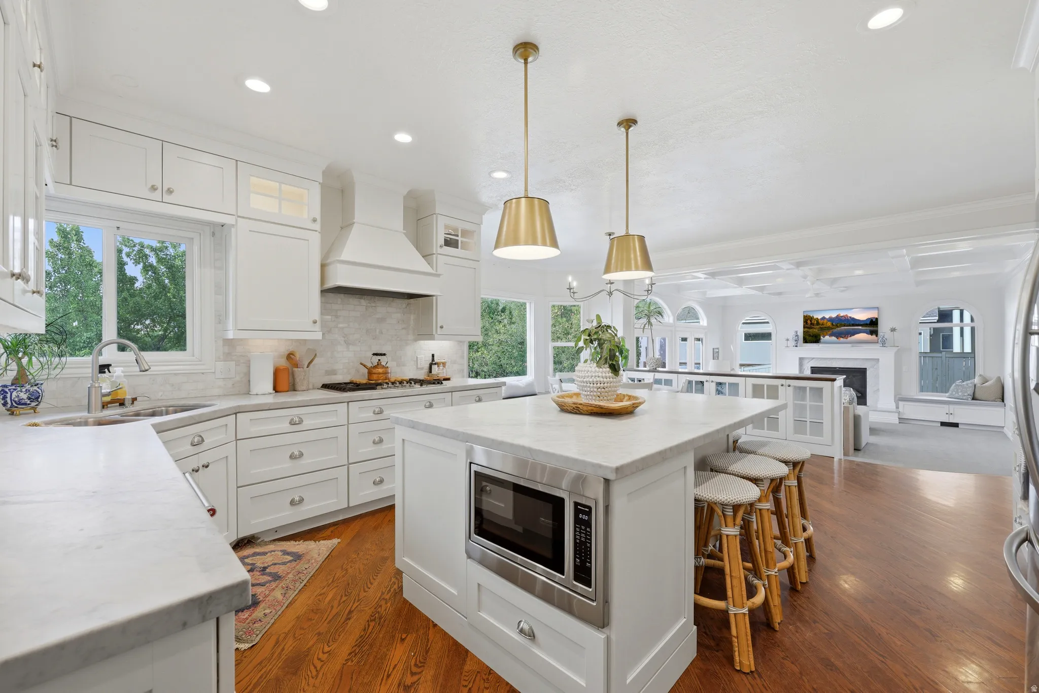 Open-concept kitchen featuring an oversized island with seating, white cabinetry, integrated stainless steel appliances, and wood-finish flooring