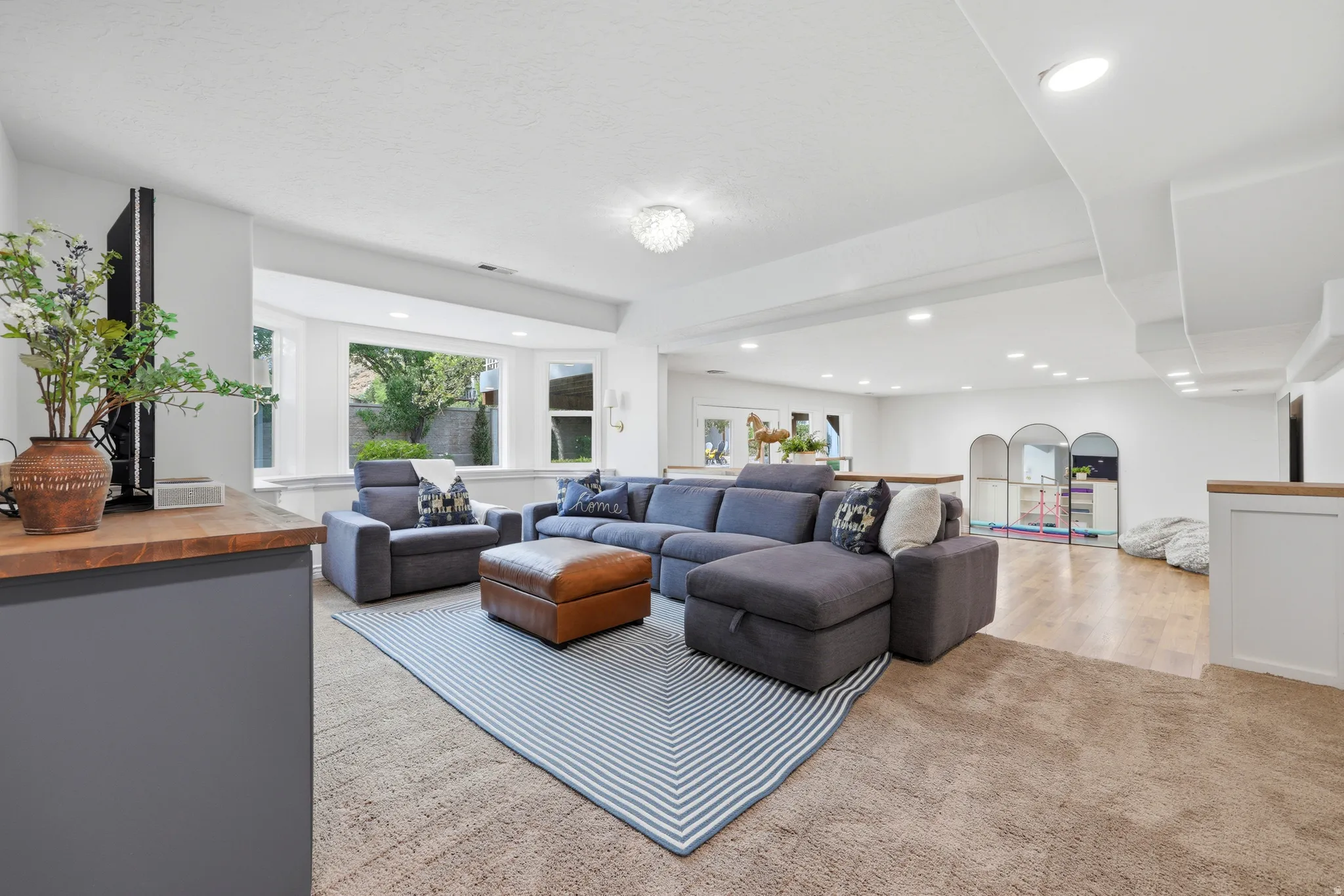 Expansive lower-level living space featuring recessed lighting, a bay window, wood-finish flooring, and a built-in wood-top counter