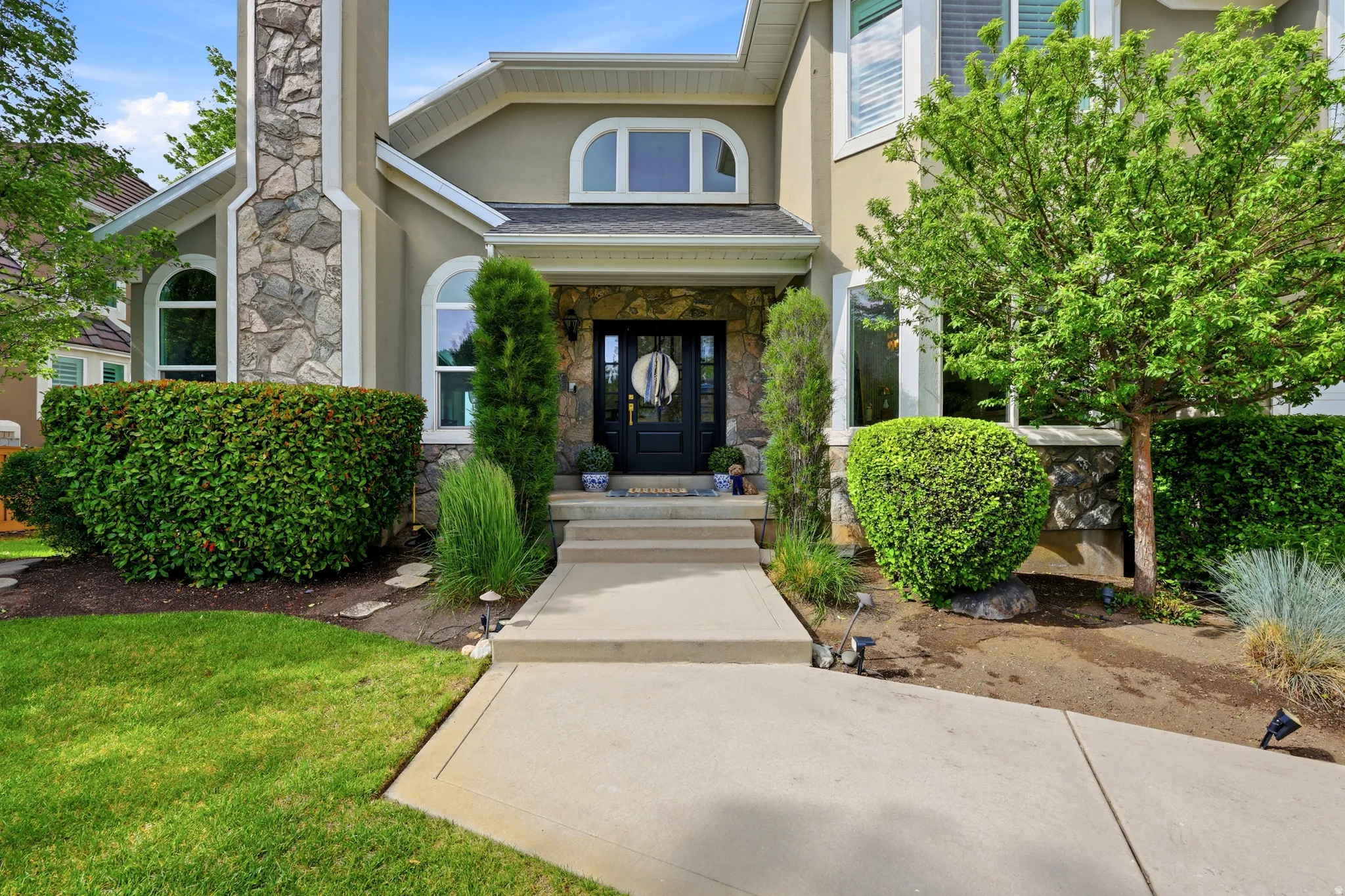Stucco exterior featuring stone accents, arched windows, and a black paneled entry door with sidelights