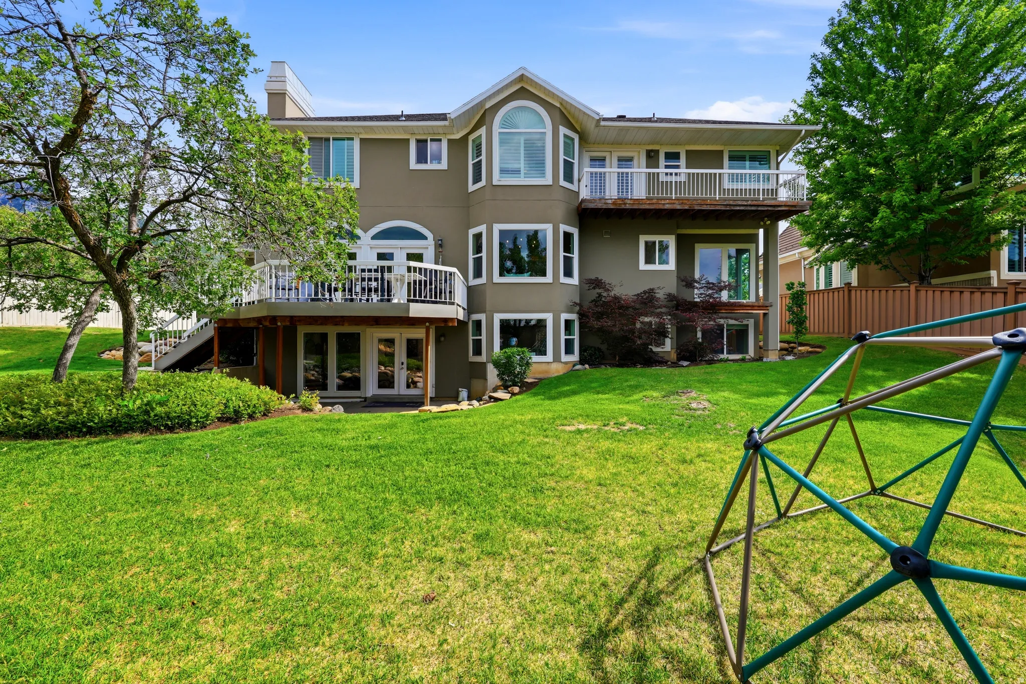 Multi-level residence featuring a neutral-toned exterior, multiple decks with white railings, and an expansive lawn