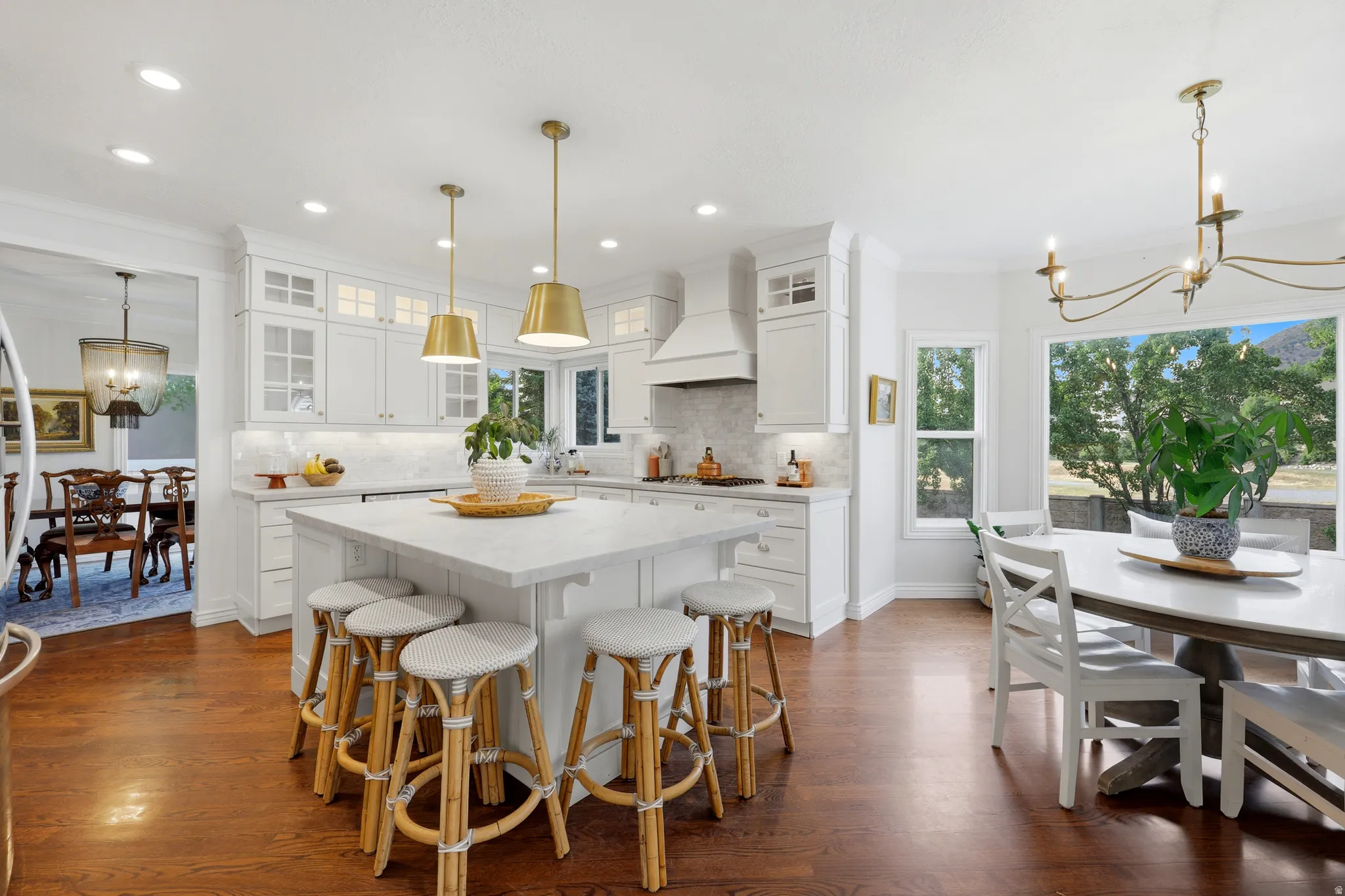 Bright kitchen featuring a substantial island with seating, white shaker cabinetry, an integrated range hood, and wood-finish flooring