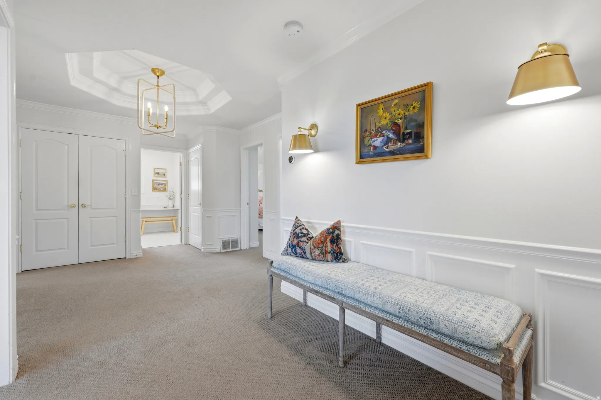 Hallway featuring a decorative ceiling tray, a gold-toned chandelier, and wall sconces