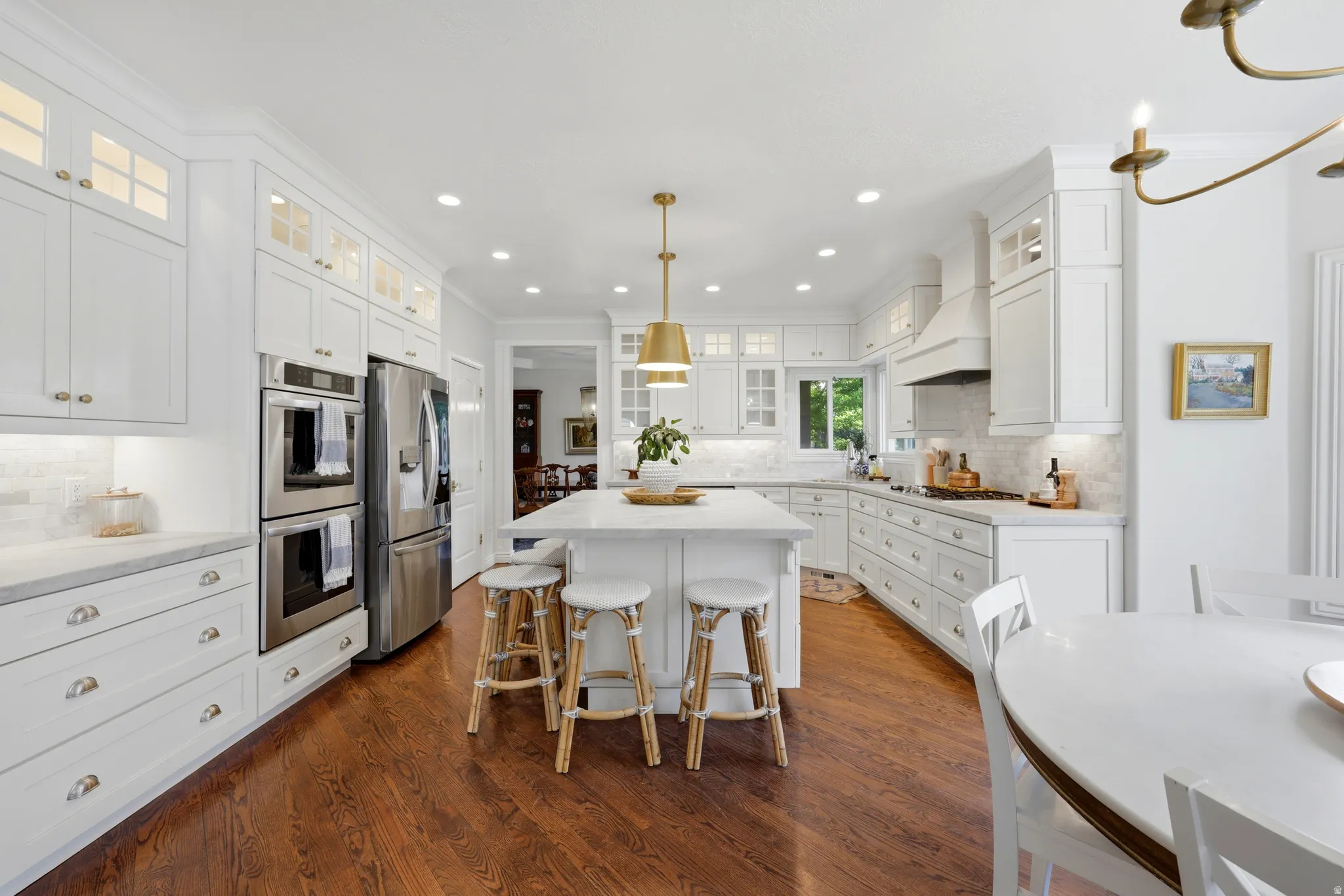 Gourmet kitchen featuring a central island, integrated stainless steel appliances, white cabinetry with upper glass-front accents, light-toned countertops, and rich wood-finish flooring