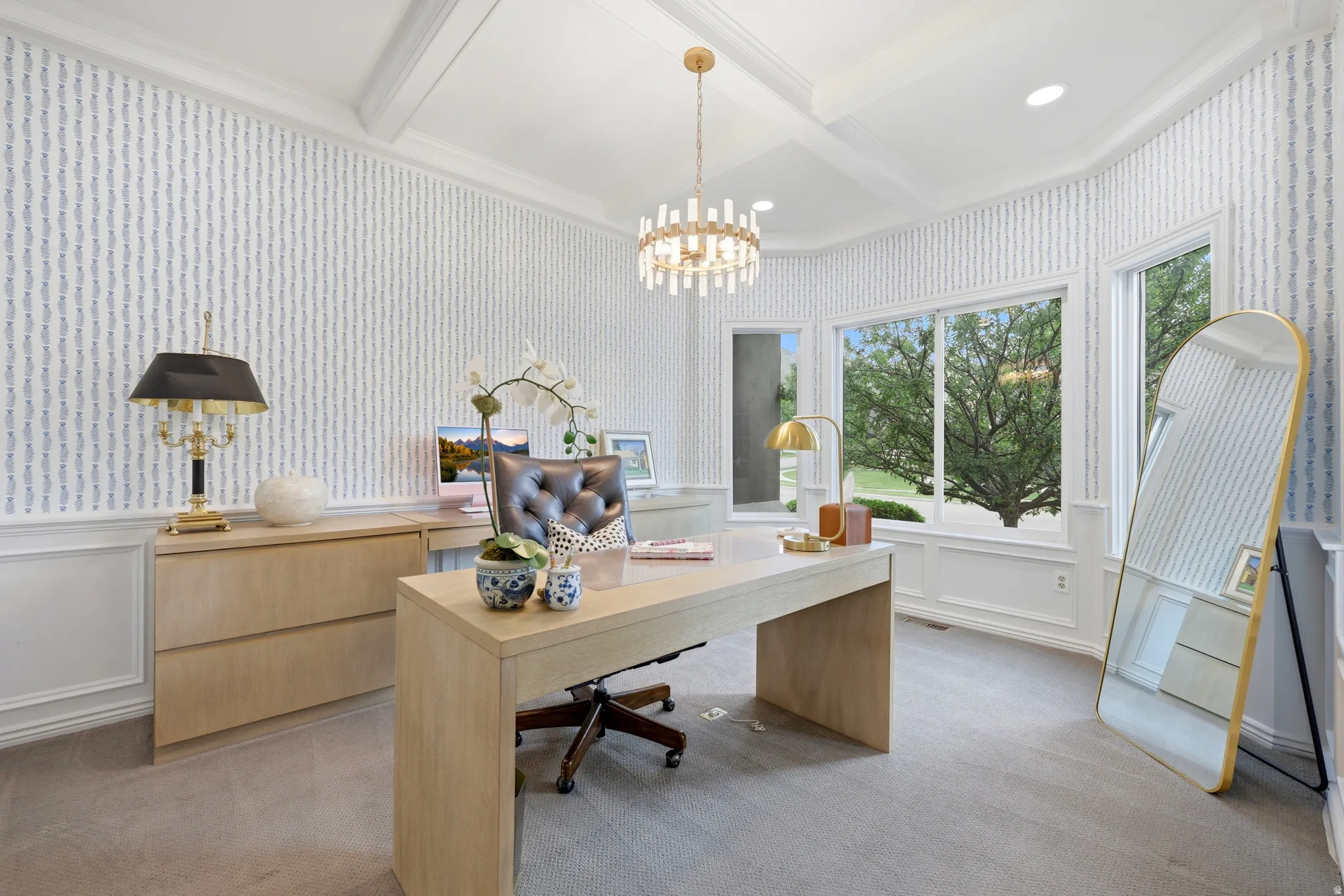 Spacious room featuring broad windows with views of mature trees, a detailed coffered ceiling, and wainscoting