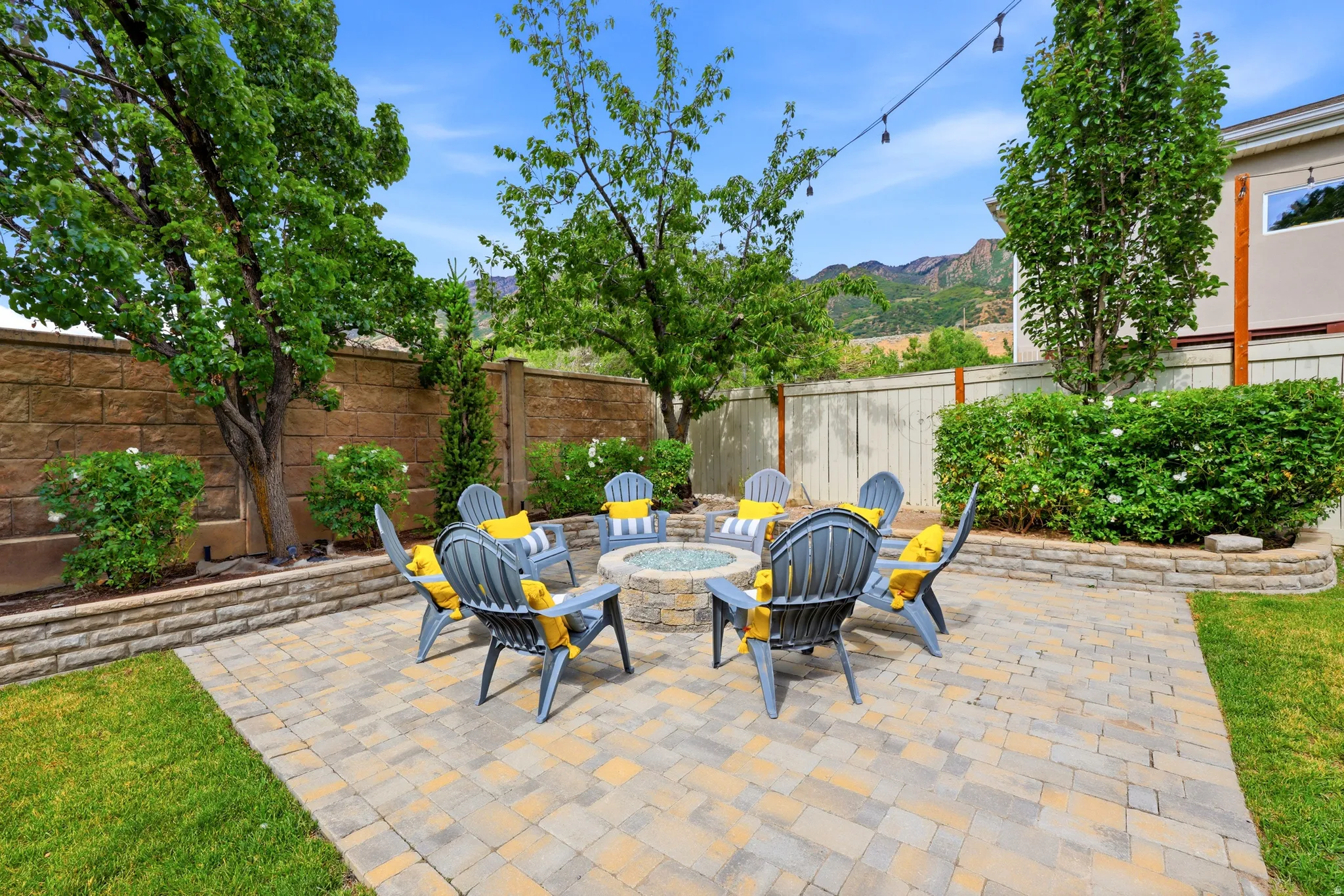 Paver patio featuring a built-in fire pit, surrounded by a stone retaining wall and mature trees