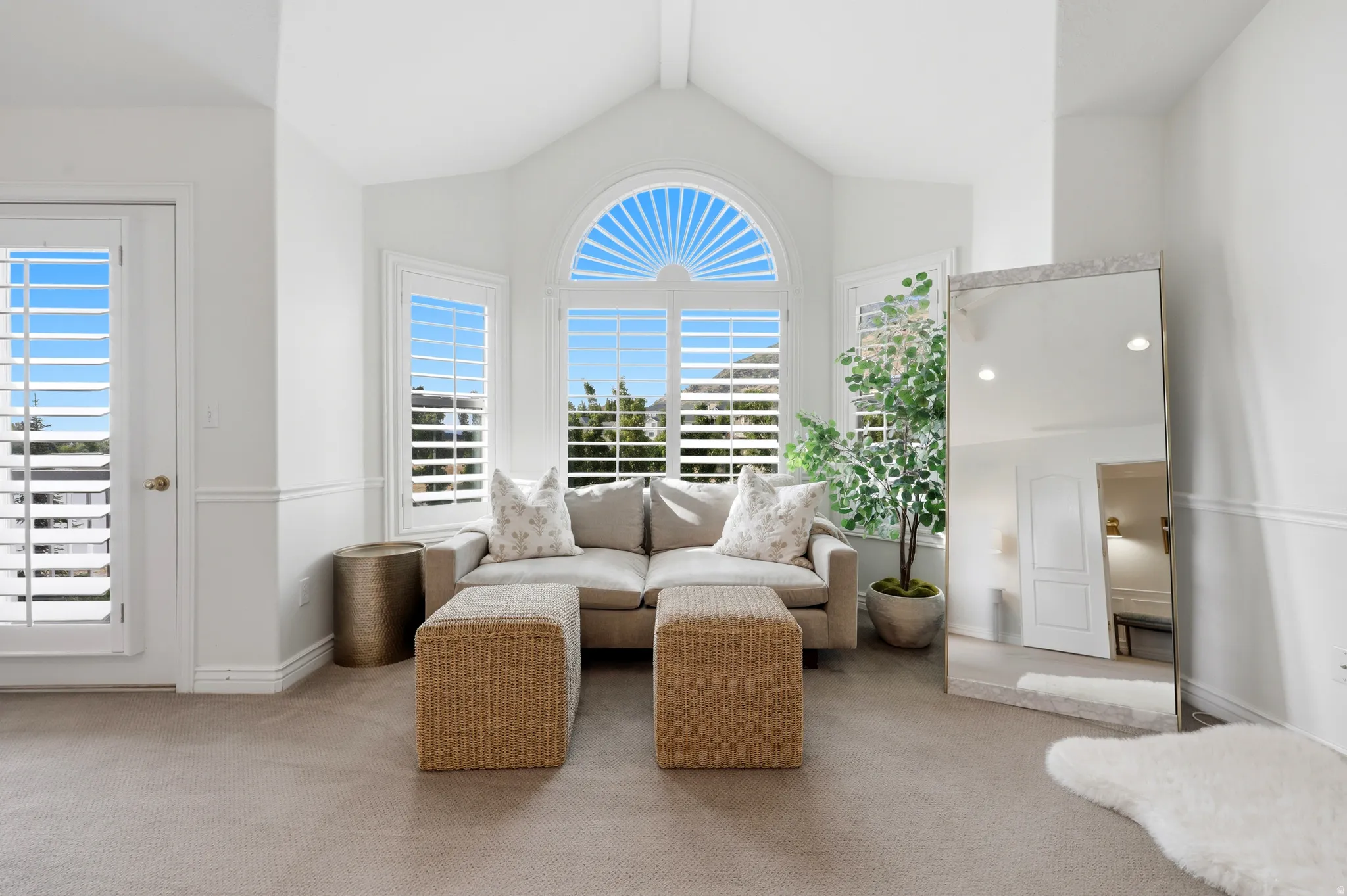 Vaulted ceiling sunroom featuring multiple windows with plantation shutters, a rounded architectural window, white baseboards, and neutral carpeting
