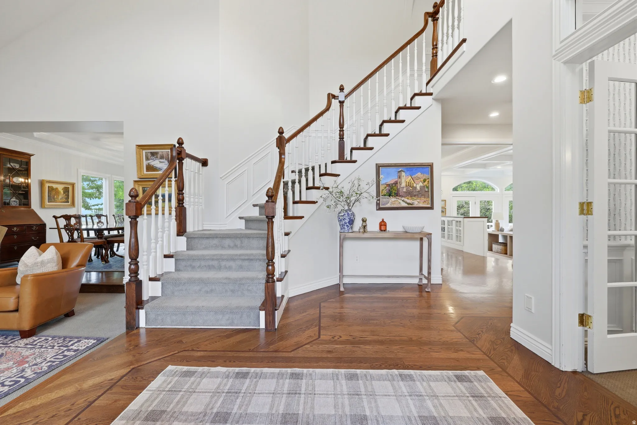 Grand entryway featuring a prominent staircase with wood-finish handrails and white balusters, wood-finish flooring with a decorative inlay, high ceilings, and French doors