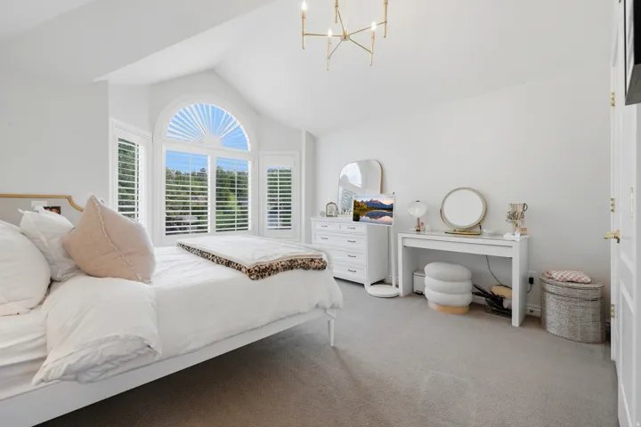 Vaulted ceilings featuring a chandelier, large arched window with plantation shutters, multiple windows, and light-toned carpeting