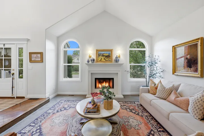 Vaulted ceilings enhance this living area, featuring a central fireplace with a classic mantel, flanked by two arched windows