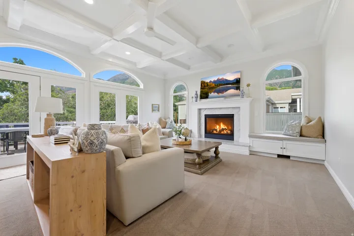 Spacious living area featuring a coffered ceiling, a marble-surround fireplace, arched windows, and double French doors opening to an outdoor patio
