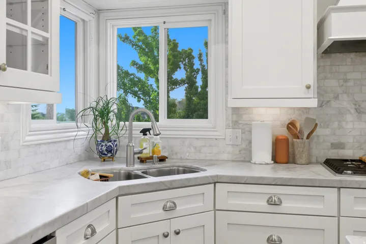Corner kitchen sink with a gooseneck faucet, set within white countertops