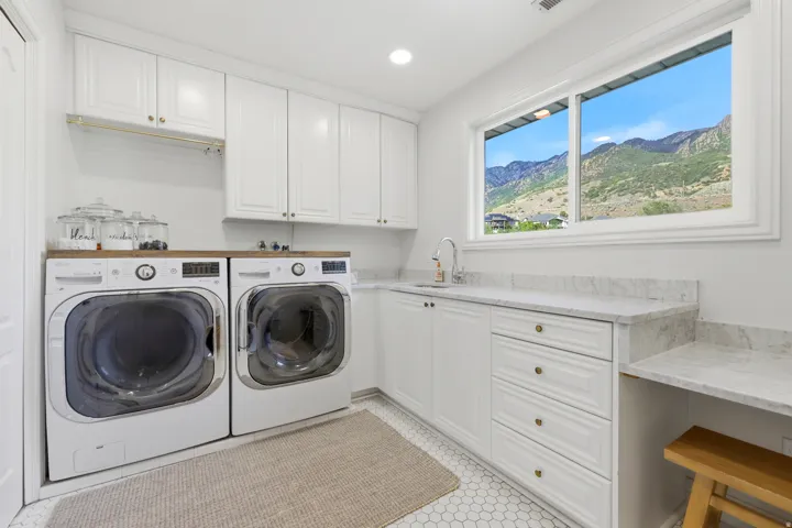 Bright laundry room featuring white cabinetry, a wood-finish countertop, and a built-in sink with a gooseneck faucet