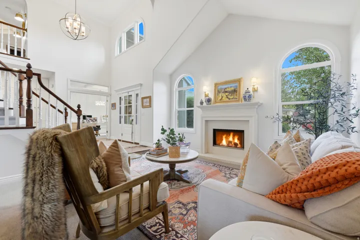 Vaulted ceiling living area featuring a built-in fireplace with a stone surround, arched windows, a multi-tiered chandelier, and a wood-finish staircase with white balusters