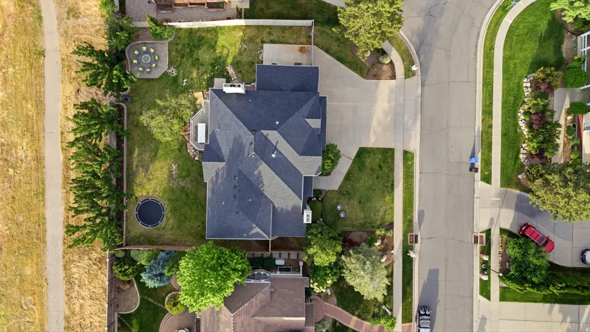 Overhead view showcasing a property with a dark shingle roof, a concrete driveway, and a backyard featuring a fire pit area