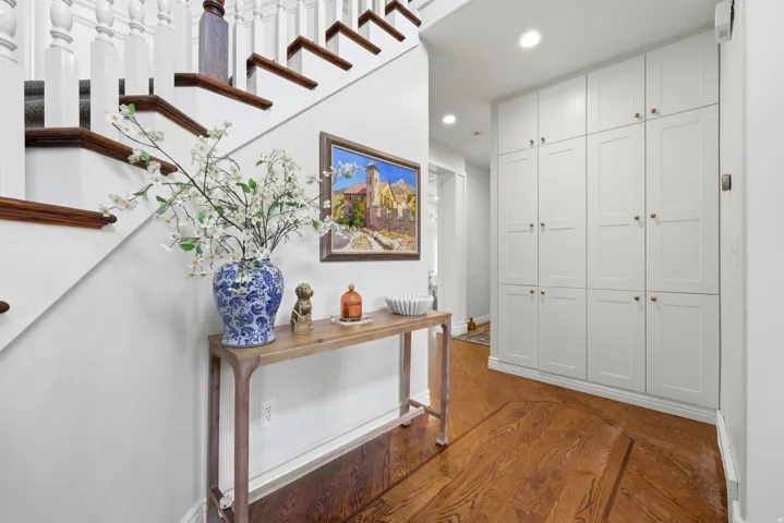 Hardwood flooring with a geometric inlay pattern, built-in white paneled cabinetry, staircase with white balusters and dark wood treads, white wall finishes, recessed lighting