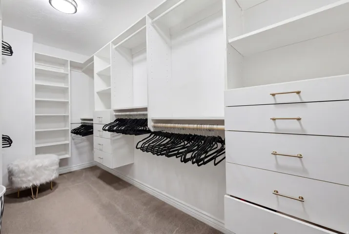 Custom closet system featuring white cabinetry, multiple hanging rods, integrated shelving units, and drawer storage with gold-tone hardware