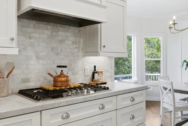Gourmet kitchen featuring a stainless steel gas range, white shaker cabinetry with polished chrome hardware, and a subway tile backsplash