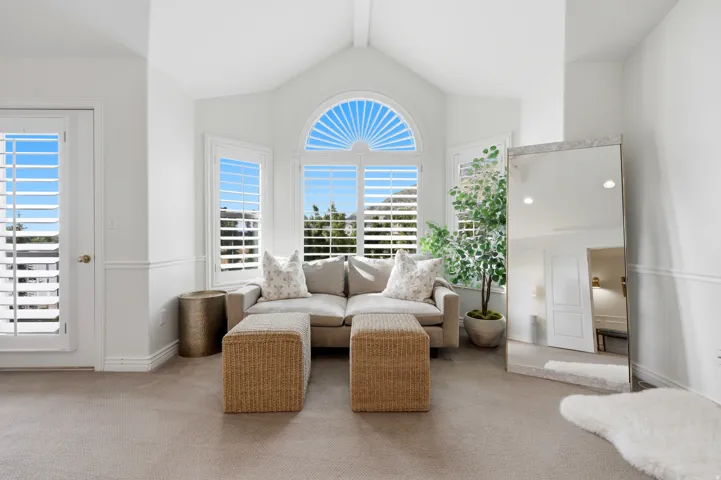 Vaulted ceiling sunroom featuring multiple windows with plantation shutters, a rounded architectural window, white baseboards, and neutral carpeting