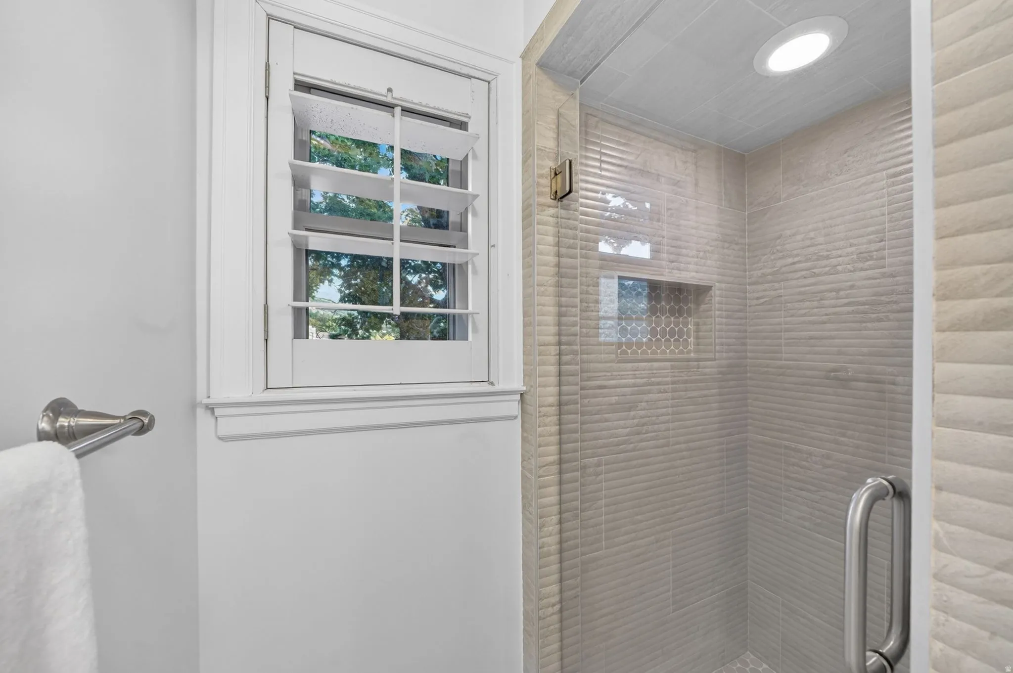 Glass-enclosed shower featuring textured wall tiles, a mosaic-tiled niche, and a recessed ceiling light