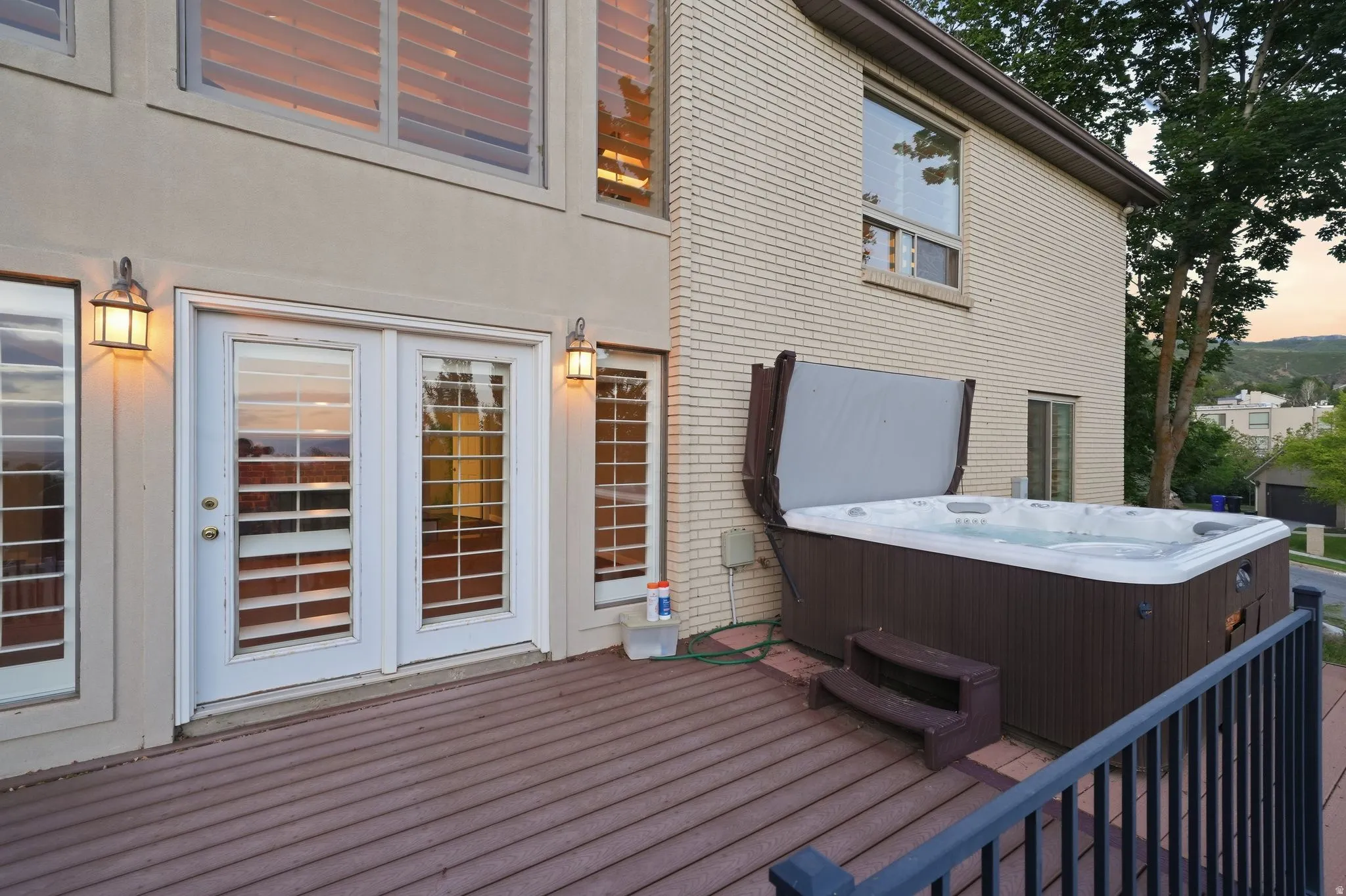 Spacious outdoor deck featuring a hot tub with cover, composite decking, white double patio doors, and exterior wall lanterns