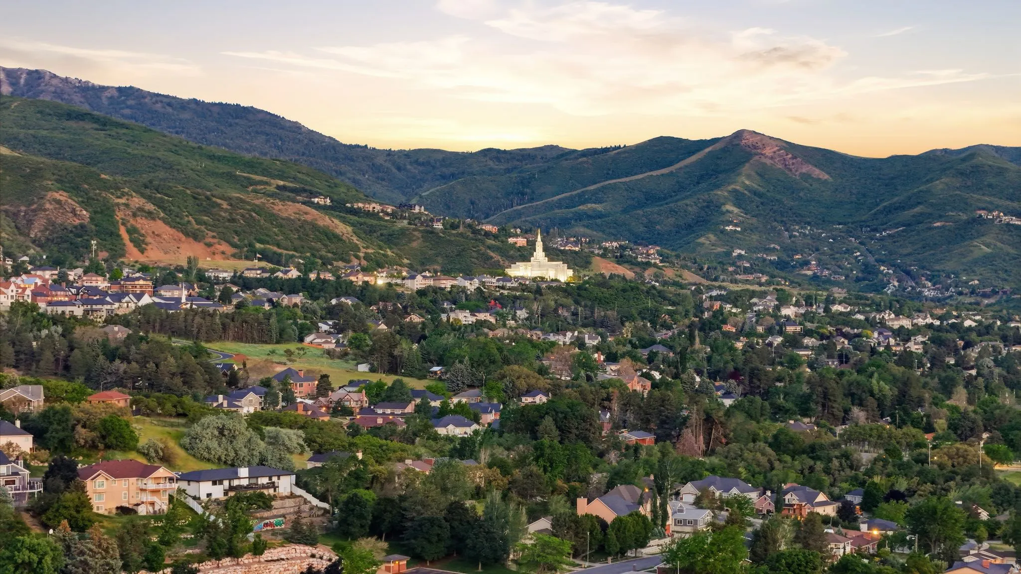 Expansive mountain landscape featuring a white spire structure, a residential community, and extensive tree coverage