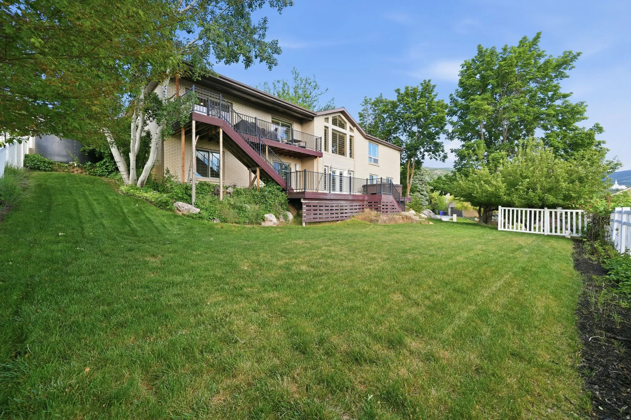 Spacious rear yard with a tiered composite deck, external staircase, and mature trees