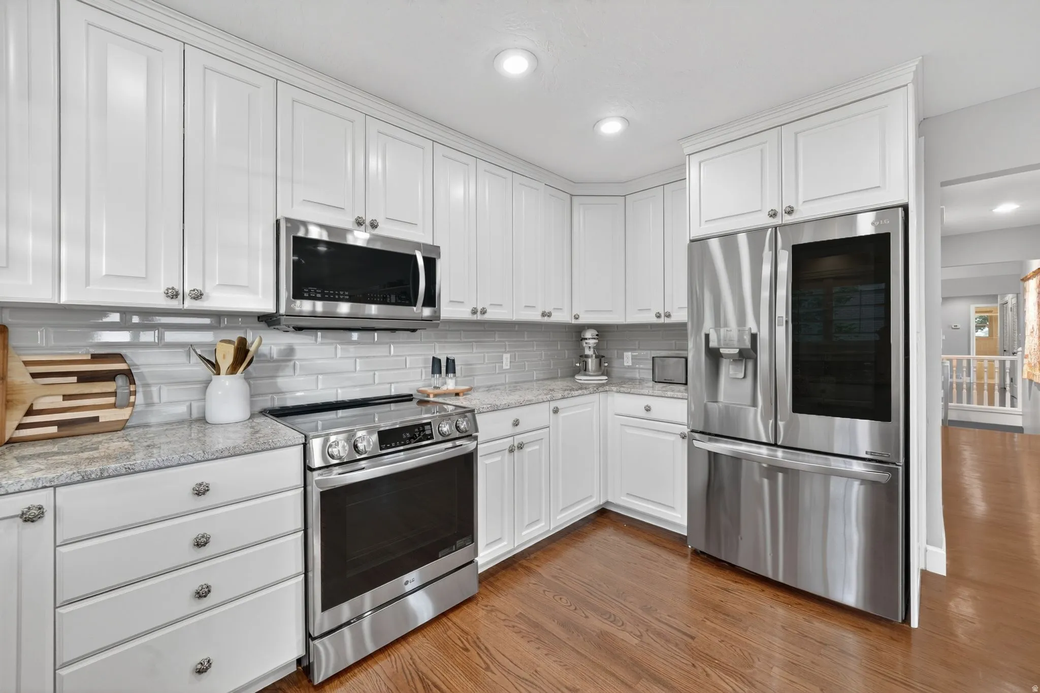Kitchen featuring white shaker-style cabinetry, stainless steel appliances, light-colored countertops, a tile backsplash, and wood-finish flooring