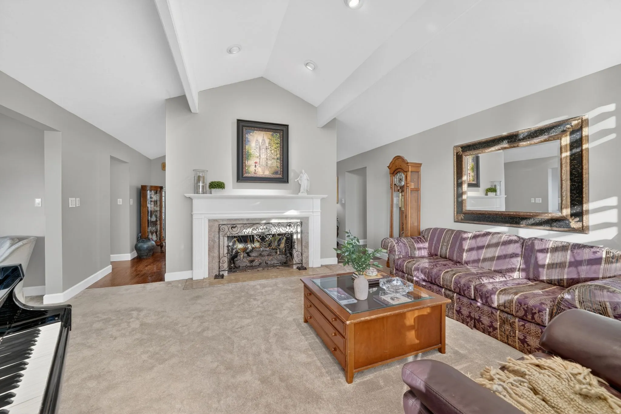 Living area featuring a fireplace with a decorative mantel, vaulted ceilings with exposed beams, recessed lighting, and a blend of carpet and wood-finish flooring