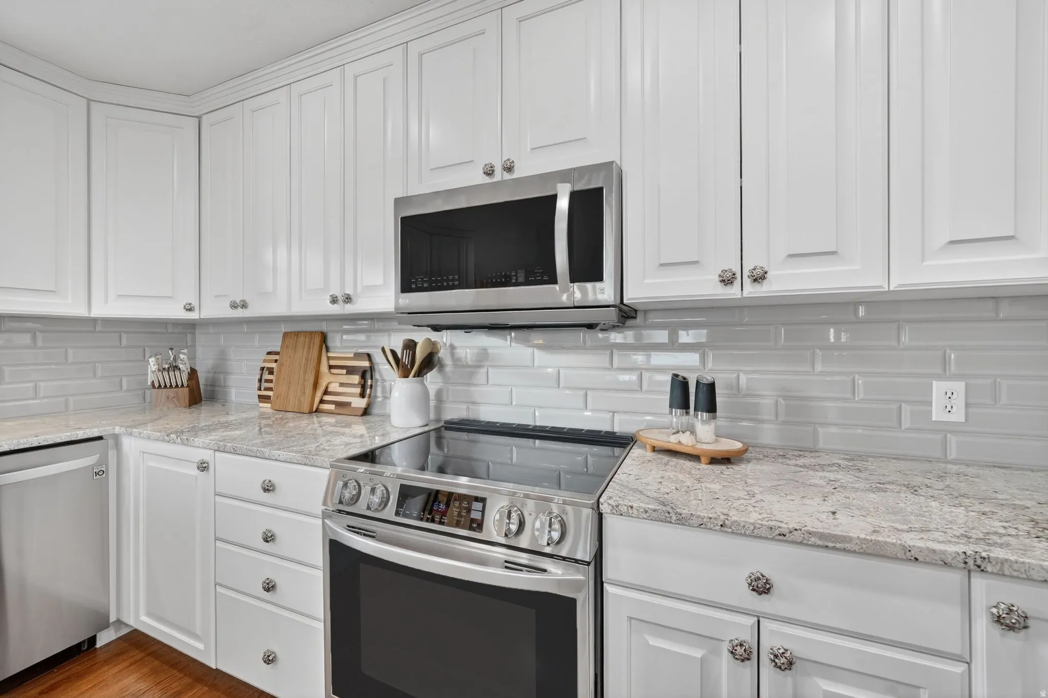 Modern kitchen featuring white shaker cabinetry, stainless steel appliances, light granite countertops, and a subway tile backsplash