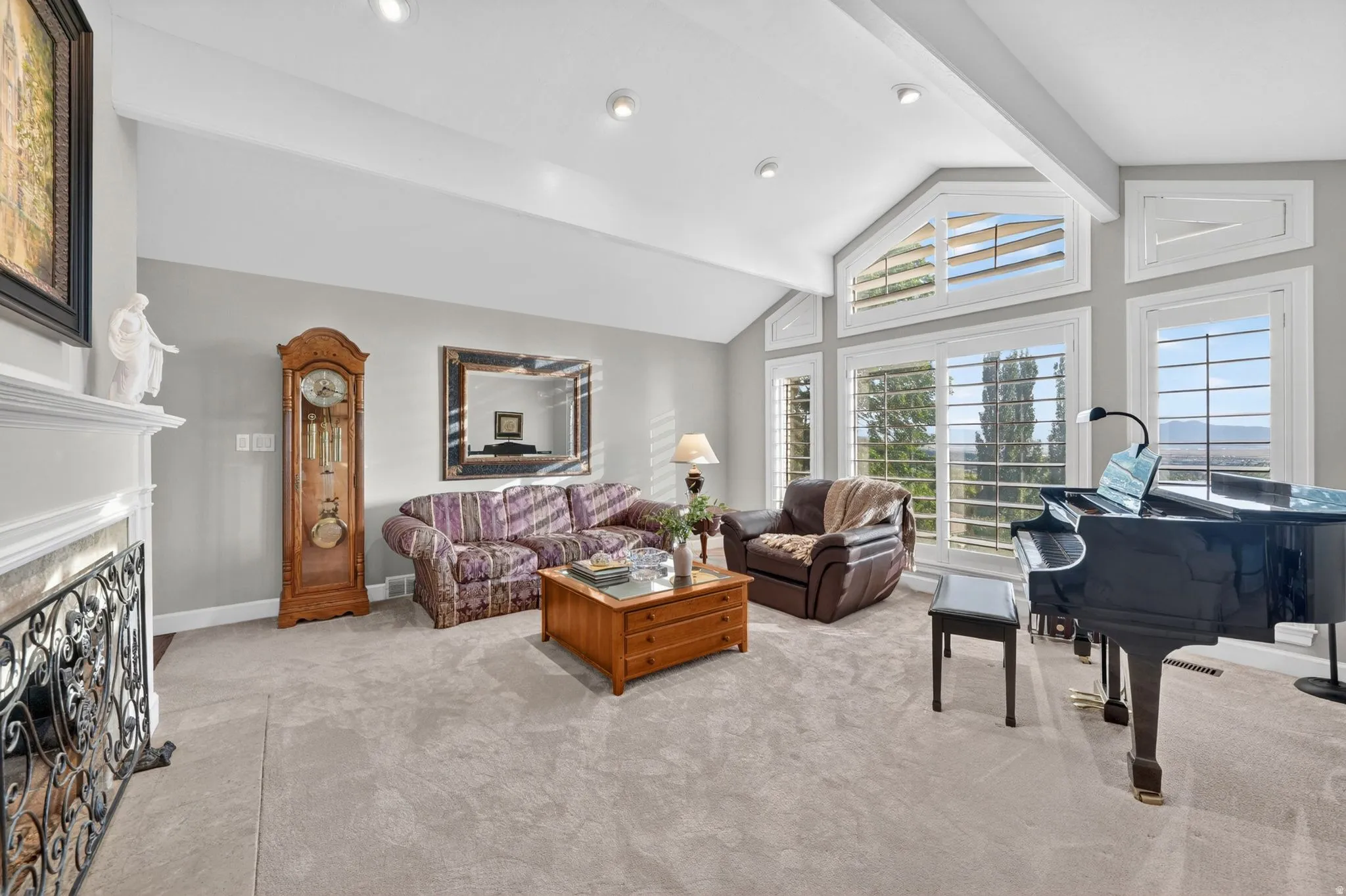 Spacious living area featuring vaulted ceilings with exposed beams, recessed lighting, and large windows with plantation shutters