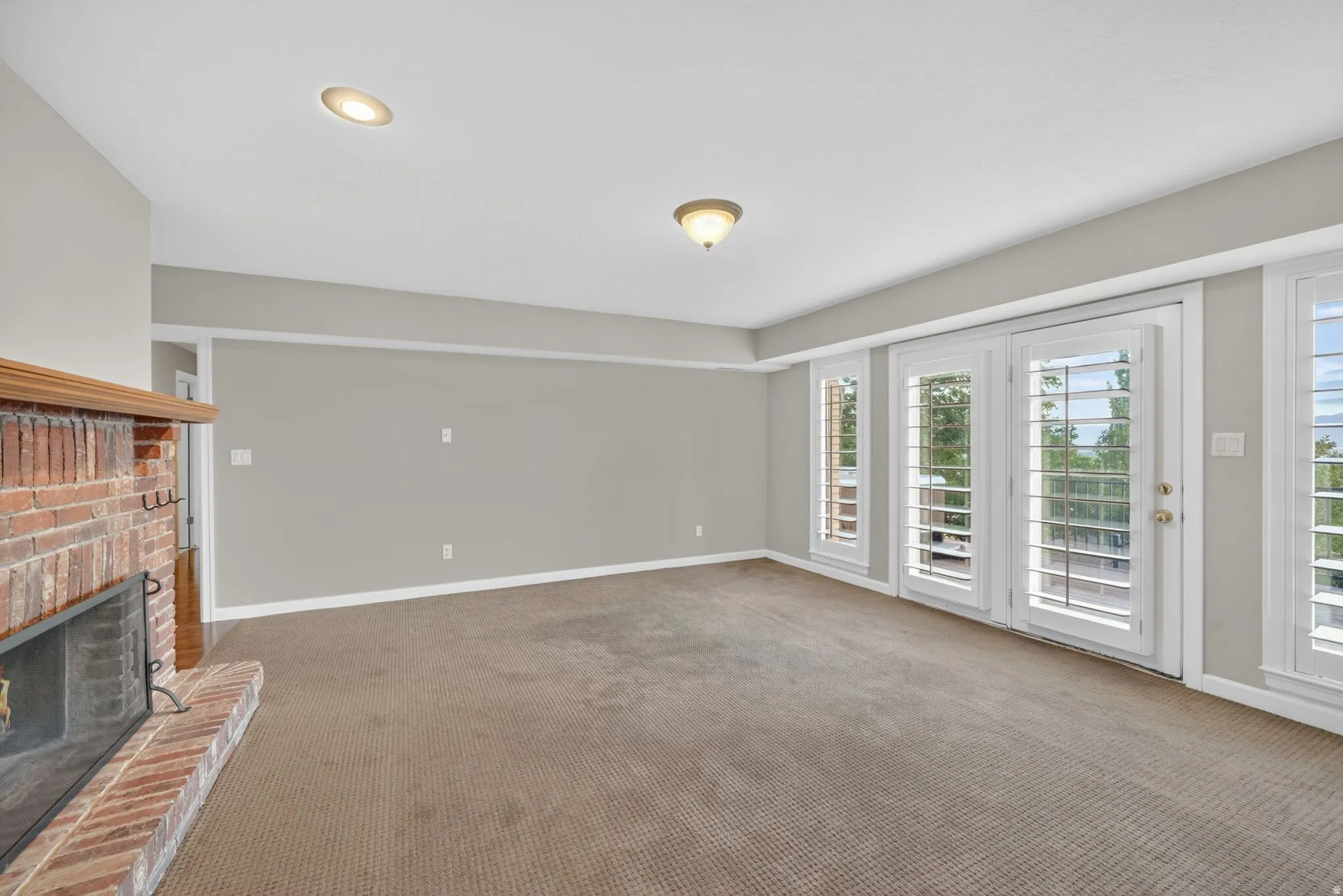 Living area featuring a brick fireplace with wood mantel, multiple windows with white plantation shutters, and recessed ceiling lighting