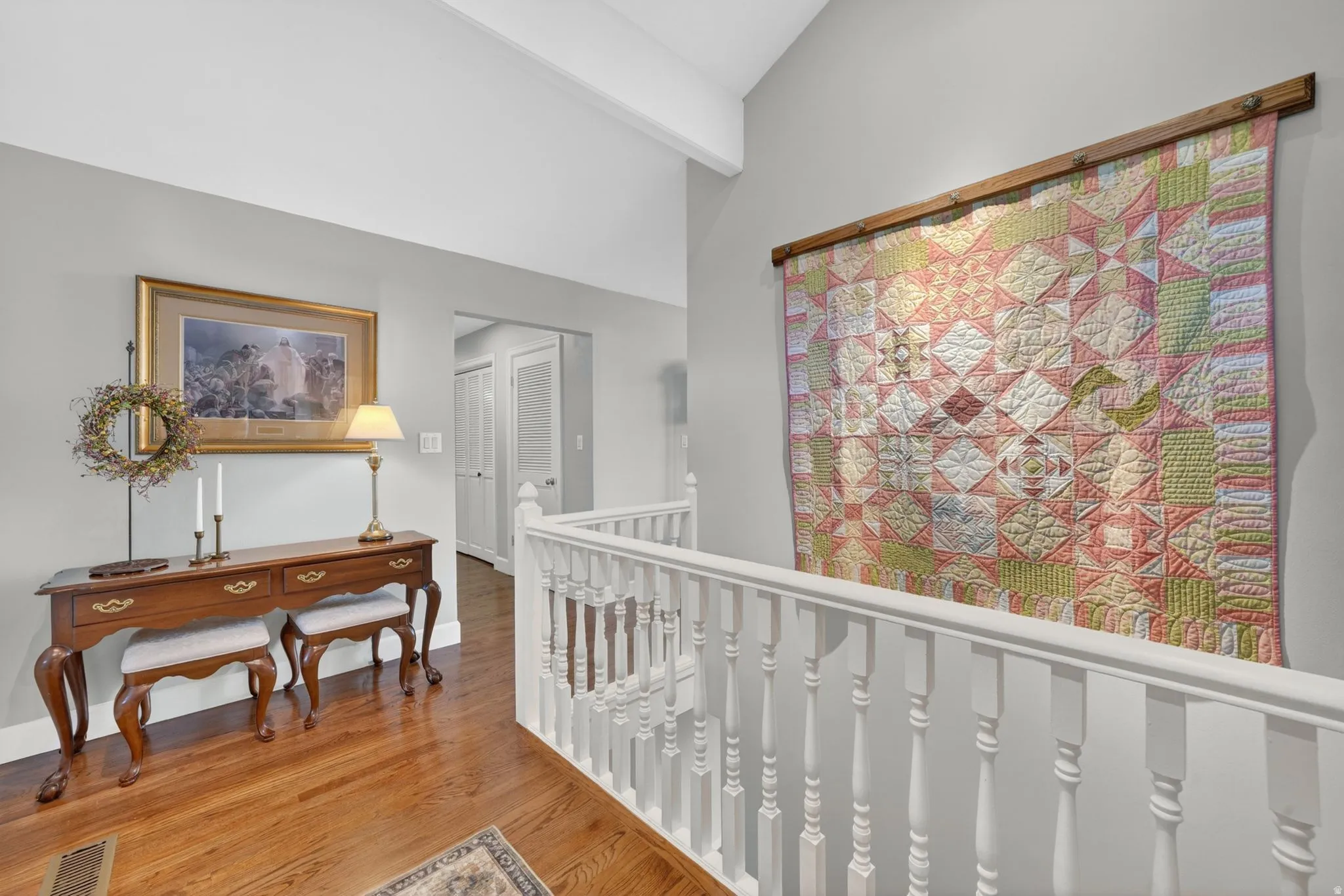 Hardwood flooring extends throughout this upper-level hallway, complemented by a white spindle railing and a vaulted ceiling with exposed beam