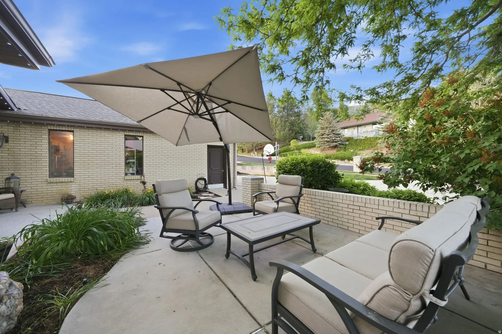 Concrete patio featuring a brick retaining wall and mature landscaping