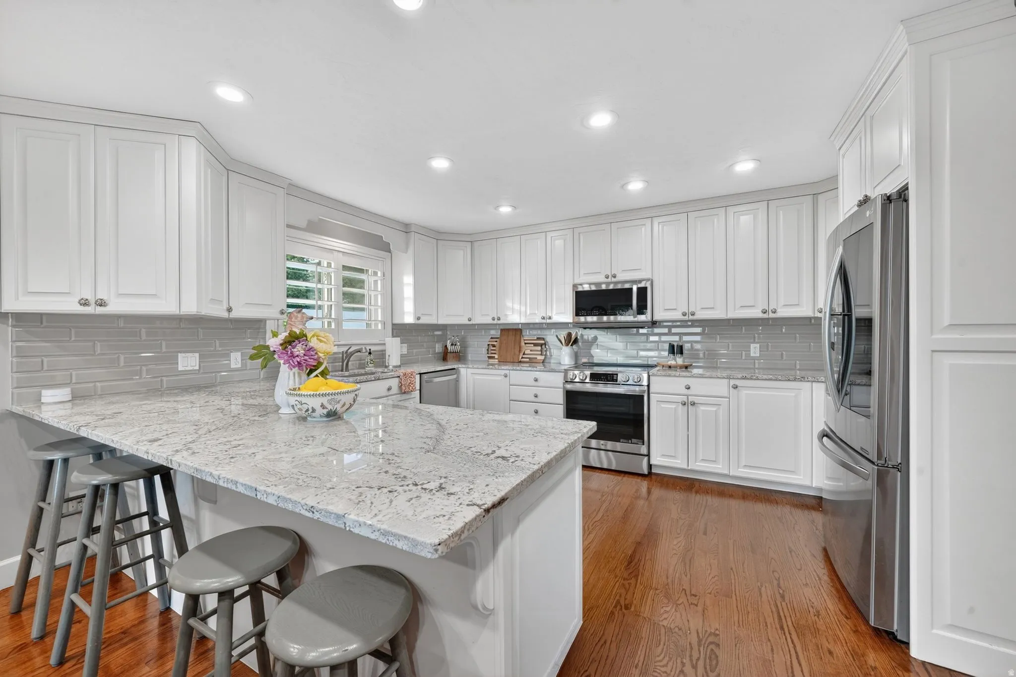 Bright kitchen featuring a substantial island with stone countertop, white shaker cabinetry, stainless steel appliances, and a gray subway tile backsplash