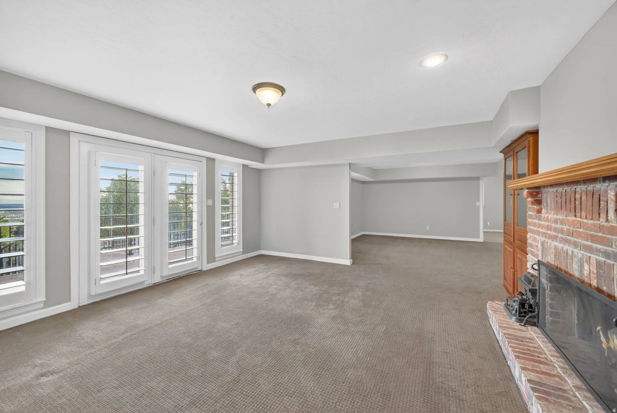Spacious interior room featuring a brick fireplace, built-in wooden cabinetry, recessed lighting, and multiple windows with plantation shutters