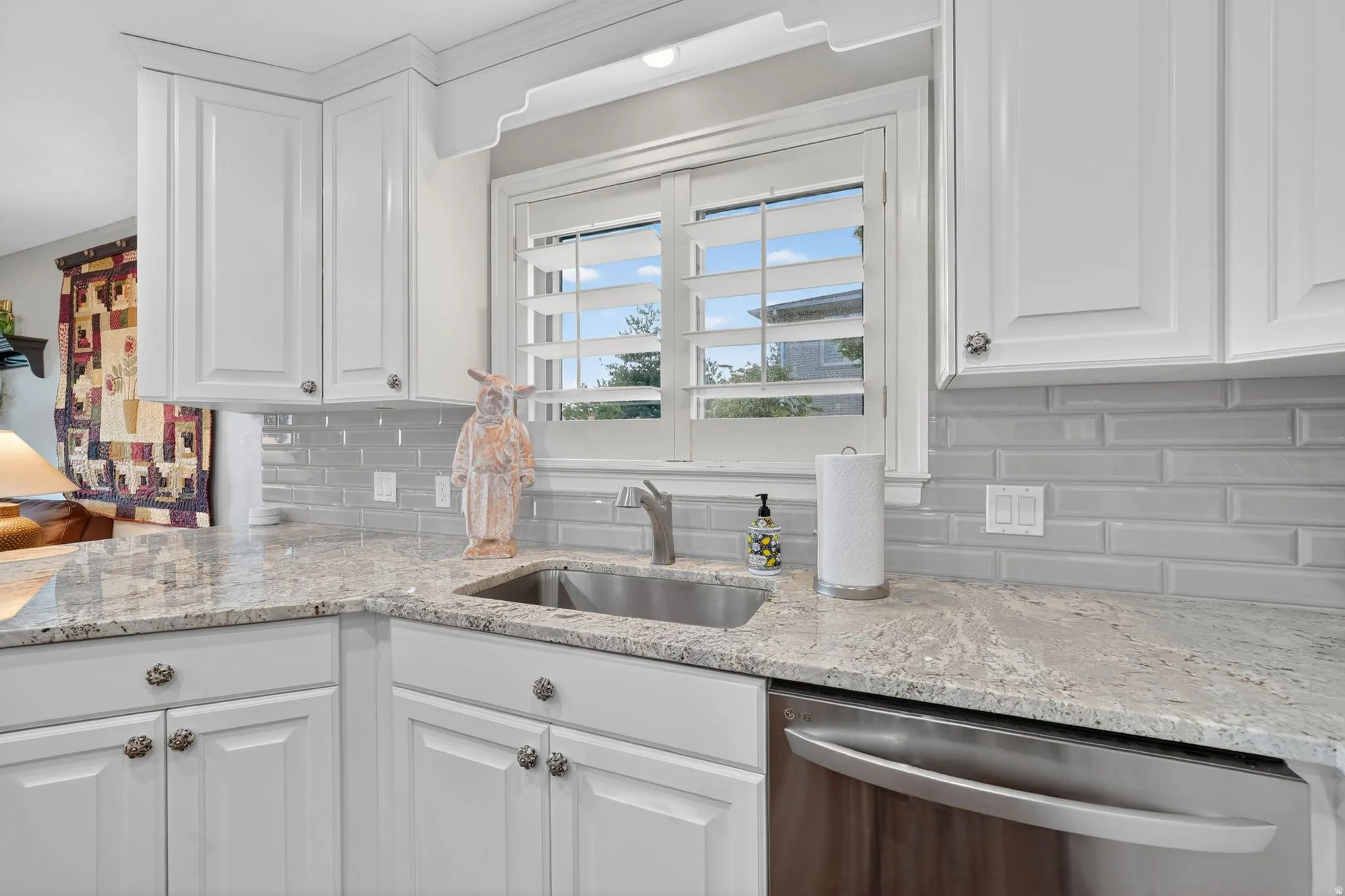 Kitchen area featuring white cabinetry, light granite countertops, a stainless steel sink, subway tile backsplash, and a built-in stainless steel dishwasher