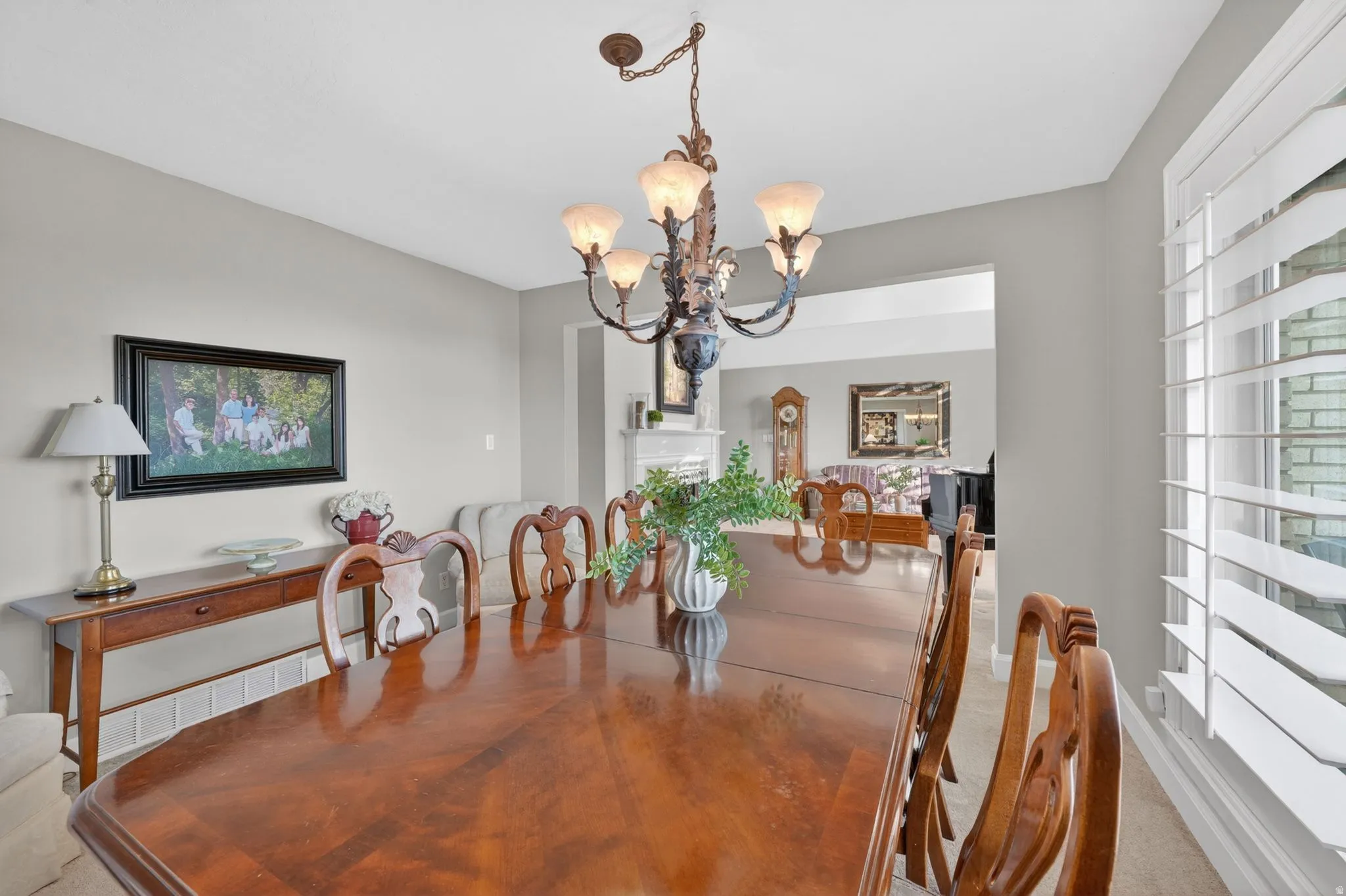 Formal dining area featuring a prominent chandelier, wood-finish flooring, and a large window with white plantation shutters