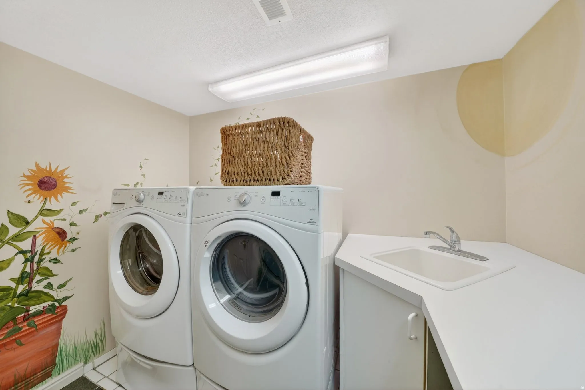Dedicated laundry area featuring a white front-loading washer and dryer, a corner countertop with an integrated sink, and white cabinetry