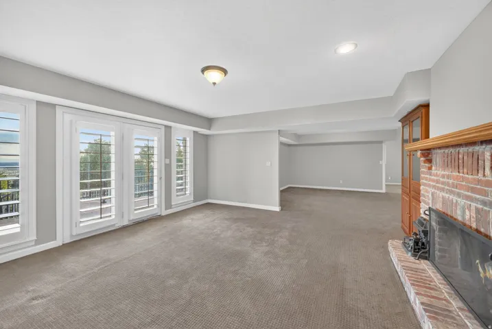 Spacious interior room featuring a brick fireplace, built-in wooden cabinetry, recessed lighting, and multiple windows with plantation shutters