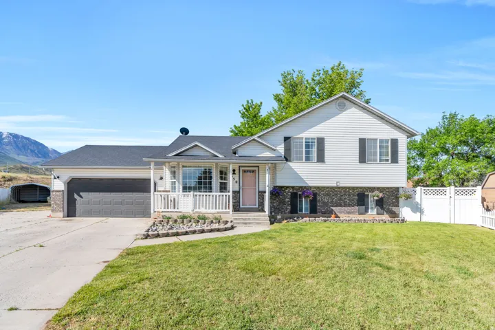 Split-level residence featuring a two-car garage, front porch with white railing, and a manicured lawn