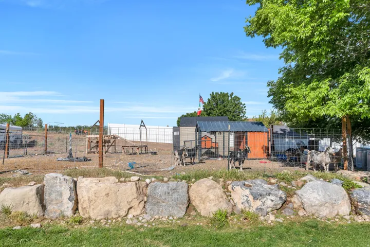 Expansive outdoor area featuring a large fenced enclosure, multiple outbuildings, mature tree, and a rock retaining wall