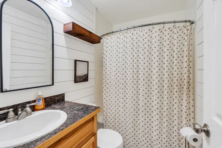 Bathroom featuring shiplap wall paneling, a wood-finish vanity with an integrated sink, and a speckled countertop